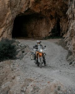 person riding motorbike on dirt road with tunnel in rocks behind